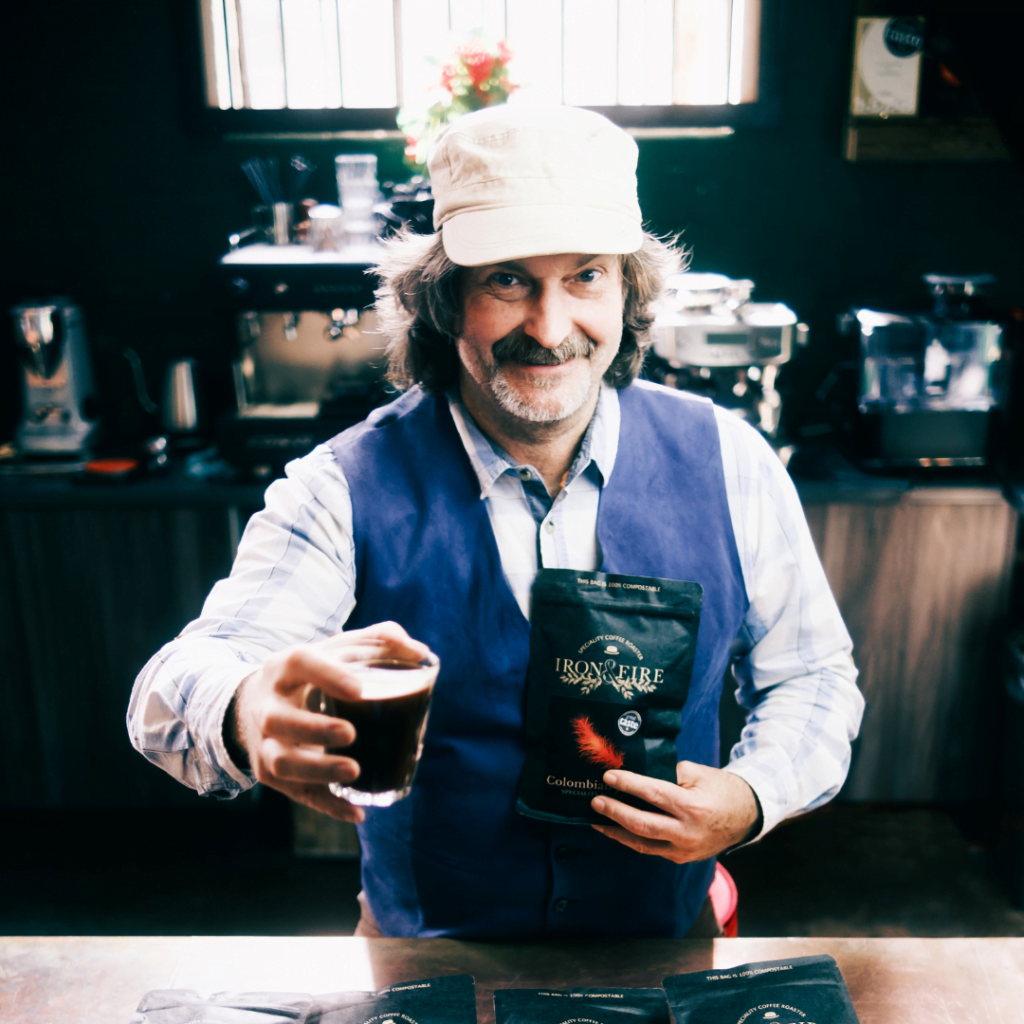 Kev, Iron & Fire co-owner, holding a glass of coffee and a bag of beans