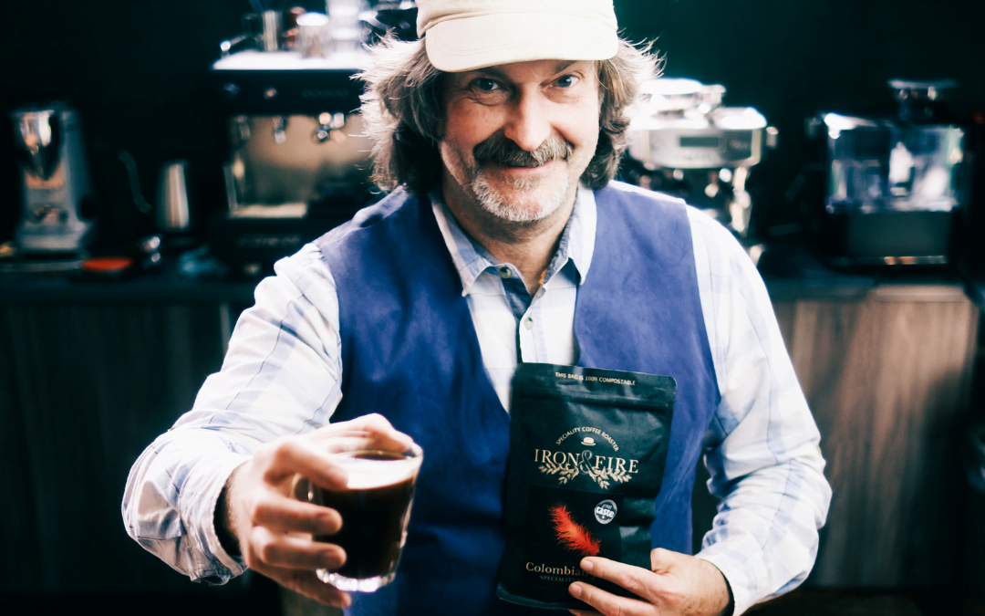 Kev, Iron & Fire co-owner, holding a glass of coffee and a bag of beans